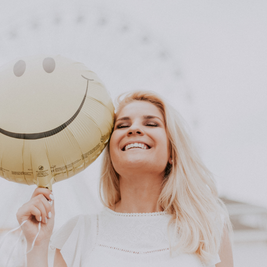 Mujer sonriendo con un globo de emoji feliz, representando los beneficios de sonreír y su impacto positivo en el bienestar emocional