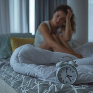 Mujer con insomnio sentada en la cama de madrugada, con un reloj despertador en primer plano.