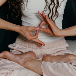 Mujer meditando en posición de loto haciendo mudra de manos, ilustrando la práctica de mantras y respiración para calmar la ansiedad.