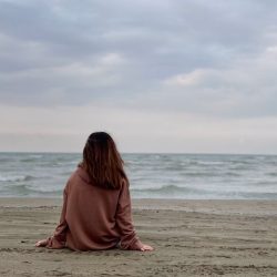 Cómo elegir una buena psicóloga en Alella: mujer sentada de espaldas mirando al mar en un momento de reflexión