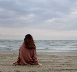 Cómo elegir una buena psicóloga en Alella: mujer sentada de espaldas mirando al mar en un momento de reflexión